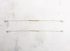 Two bracelets, one gold and one silver displayed on a marble board. Both bracelets feature a textured “twig” bar suspended in the middle of a fine chain